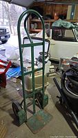Front view of green metal hand truck with safety-loop handle in garage setting.
