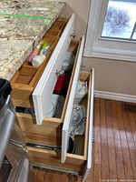 View of open kitchen drawers showing organized wooden drawer inserts holding kitchen utensils such as spatula, whisk, bottle stopper, and others with some bakeware and dishes in lower drawers.