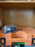 Orange plastic case for rotary laser level kit with a small boxed item on top.