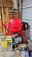 Front view of red portable concrete mixer on steel frame with motor housing and included QUIKRETE Walk Maker box in foreground.