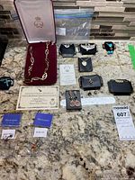Full lot of costume jewelry displayed on granite counter including necklaces in boxes, multiple pairs of earrings, and certificates.