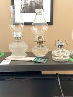 Two glass oil lamps with chimneys, one oil lamp base, and packs of extra wicks on table