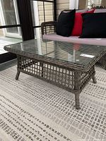 Side angle view of rectangular patio coffee table showing woven rattan-style base and glass top with rounded edges.