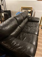 Front perspective of the black pleather 3-seat sofa with cushioned seating and backrest in a basement room.