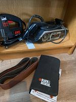 Skil variable speed jig saw and Black & Decker belt sander with sanding belts on wooden shelf.