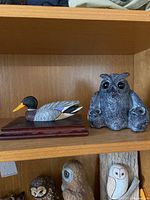 Four sculptures on wooden shelves including a duck on base and three owl sculptures below it