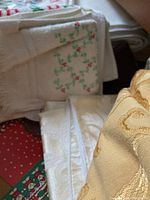 Close-up photo showing several folded linens including a white cloth with green and red embroidered vines and a thick white cloth with a damask pattern, plus a gold colored fabric.