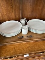 White porcelain plates and small condiment containers with lids, placed on wooden shelf
