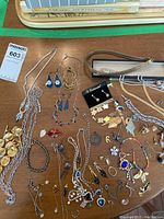 Top view of assorted vintage jewelry on wooden surface including multiple chains, earrings, rings, bracelets, and collector spoons