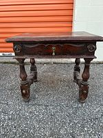 Front view of the antique wooden side table showing turned legs, carved drawer front with metal keyhole, and decorative carved stretchers