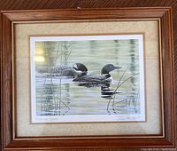 Full view of the framed print showing two loons swimming in water with reeds and wooden frame.