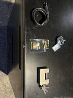 Five different locks on a flat surface: a coiled bicycle cable lock, brass padlock in box, chrome cylinder lock, and a large heavy-duty shutter lock with keys attached.