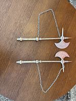 Top view of two ornate decorative metal axes connected by a chain, placed on a wooden surface showing detailed engraving and gilded wear.