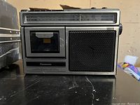 Front view of Panasonic RX-1250 boombox showing cassette tape deck, speaker, and radio tuner panel.
