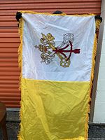 Front view of the Vatican City flag showing white and yellow halves with central printed papal keys symbol and gold fringe border.