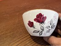 Side view of vintage semi-porcelain cup with floral rose design and 22kt gold rim on wooden surface.