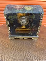 Front view of the vintage hand-painted wooden chest showing floral design, metal stud trim, scalloped base, and metal clasp.