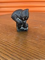 Side view of the dark soapstone carving showing the Inuit figure in a bent posture with detailed hood and clothing folds.