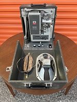 Open Kodak Pageant sound projector inside carrying case, showing mechanical parts and included speaker with wiring.