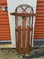 Full front view of the vintage Spartan sled showing wooden slats, metal runners, and the curved metal handle.