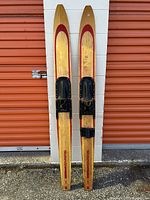 Front view of two wooden waterskis standing vertically against a white brick wall showing overall condition and bindings.