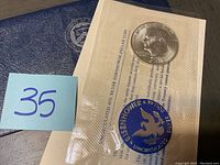 Photo showing the 1973 Eisenhower Uncirculated Silver Dollar coin sealed in original plastic packaging with informational insert and a blue eagle logo.
