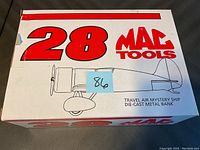 Box of 1993 Mac Tools Travel Air Mystery Ship die-cast metal bank airplane showing front and top sides with product branding and airplane illustration.