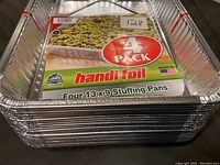 Stack of shiny silver aluminum foil pans with packaging label showing 4-pack of 13x9 stuffing pans.