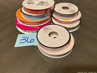 Stack of 12 craft ribbon spools showing various colors and patterns including polka dots, checks, solid colors, and some printed text.