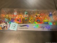Full set of 10 Disney 100 Years Laughter collectible figurines inside clear plastic packaging, including characters such as Pascal, Forky, Rapunzel, Jiminy Cricket, José Carioca, Goofy, Alien, and Dory.