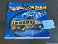 Blue Hot Wheels Hauler packaging showing school bus style die-cast truck with black and yellow details, six wheels, sealed in new condition.