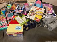Photo showing a miscellaneous box containing new items like Post-it notes, Marvel card pack, disposable cups, colorful socks, and DVDs including 'Despicable Me' and 'Firestorm'.
