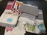 View of new dish towels and rag sets, including red and white striped towel, gray and white striped towels with fringed edges, owl print towels, and a gray quilted pot holder.