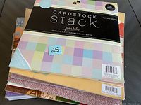 Two photos showing two separate stacks of cardstock sheets each labeled 'Cardstock Stack Pastels' with 58 sheets per pack and additional varied pattern sheets under them.
