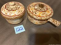 Two hand-painted ceramic kitchen pieces, a covered bowl and a small saucepan with handle, shown from top and side angles.