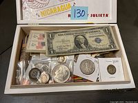 Top view of open wooden box showing US Silver Certificate note, assorted coins in flips and rolls, postage stamps in bags