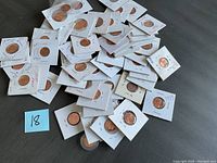 Top view of a pile of Lincoln pennies individually sleeved in white cardboard holders with circular window openings, many with handwritten date annotations.