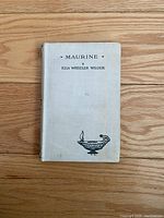 Front cover of the antique book titled 'Maurine' by Ella Wheeler Wilcox, showing cloth binding and printed text with a small graphic.