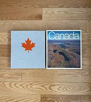 Top view of the book with slipcover showing red maple leaf on slipcover and 'Canada' title with aerial photo on book cover.