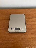 Photo of Etekcity digital kitchen scale showing stainless steel top surface with unit and tare buttons and LCD screen off.
