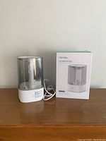 Front view of Homasy humidifier with clear water tank and white base plus original box on side