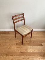 Front angled view of the mid-century teak dining chair showing the wood frame and fabric cushion.