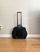Front view of black business case luggage with retractable telescopic handle fully extended and two wheels at the base.