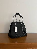 Front and side view of the black perforated Rainsmore bag on wooden surface against plain wall