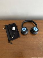Top-down view of headphones, pouch, and charger laid on wooden table showing branding and accessories.