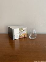 Box of Threshold wine glasses with one glass placed next to it on a wooden surface against a plain light background.