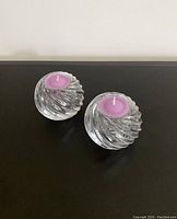 Top view of two glass spiral candle holders with pink tea light candles inside on dark surface