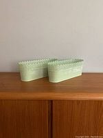 Two light green metal IKEA planters on wooden surface, showing overall shape and size.