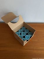 Open cardboard box showing nine blue aromatherapy candles arranged in three rows of three.