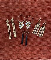 Four pairs of vintage costume jewelry earrings displayed on reddish fabric, showing variations in style including chain link clip-ons, pearl-accented hoops, filigree drops, and black dangles.